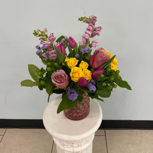 Mixed bouquet of pink, yellow, and purple flowers in a pink glass vase