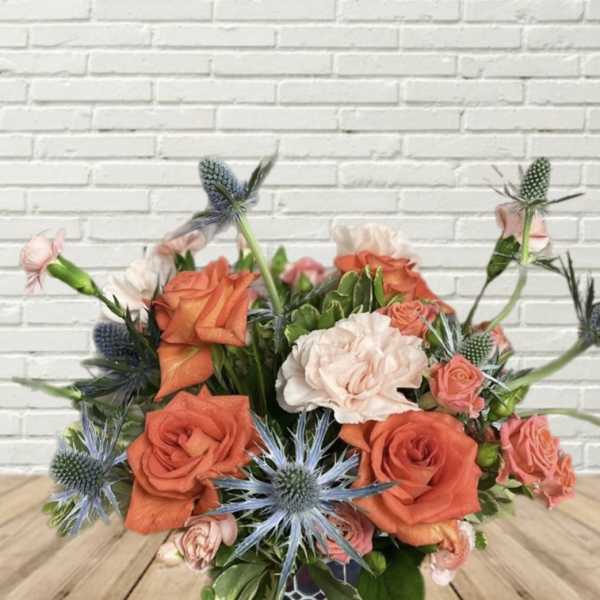 Orange and blush roses with blue thistle in a low bouquet