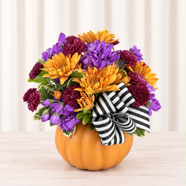 Purple and orange flower arrangement in a pumpkin container with a striped bow