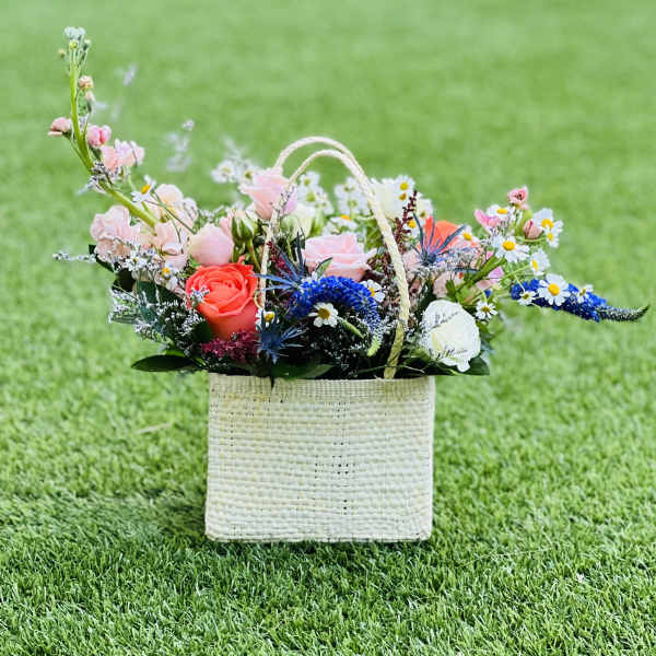 Mixed flower arrangement in a woven basket on grass
