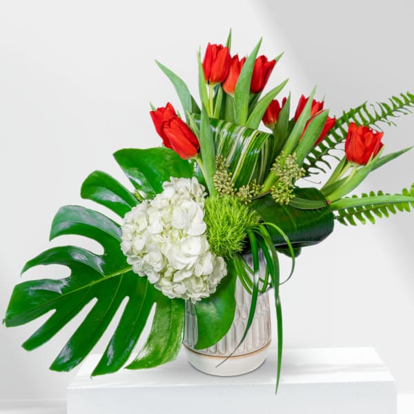 Red tulips and white hydrangea in a ceramic vase with large tropical leaves