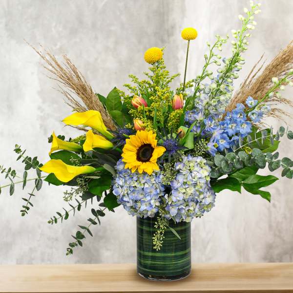 Mixed bouquet with sunflowers, calla lilies, and blue flowers in a glass vase