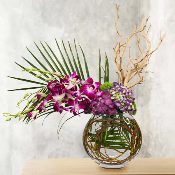 Purple orchids and hydrangeas in a glass vase with palm fronds and branches