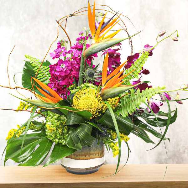 Tropical floral arrangement with orange bird-of-paradise and purple orchids in a vase