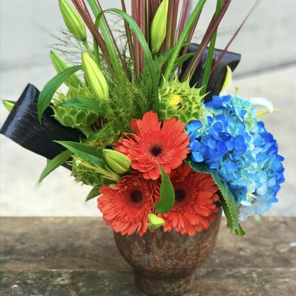 Bright mixed bouquet with red gerberas and blue hydrangea in a brown vase