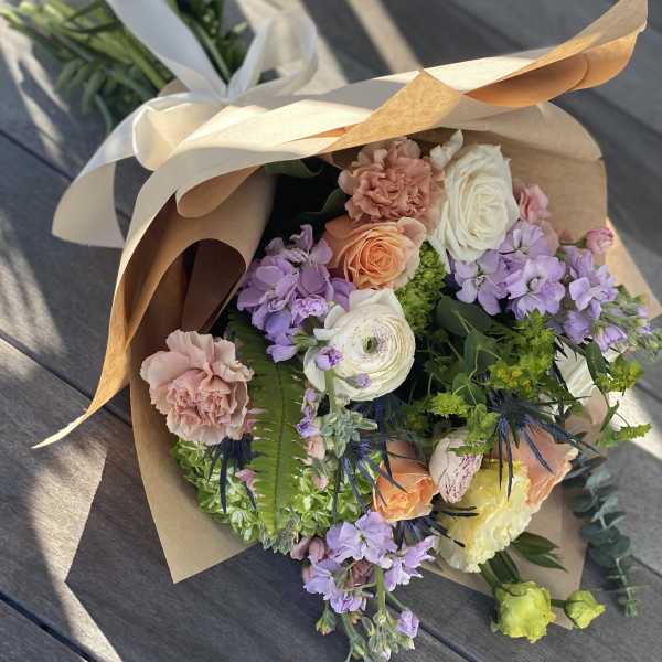 Wrapped bouquet of pastel roses, carnations, and purple blooms