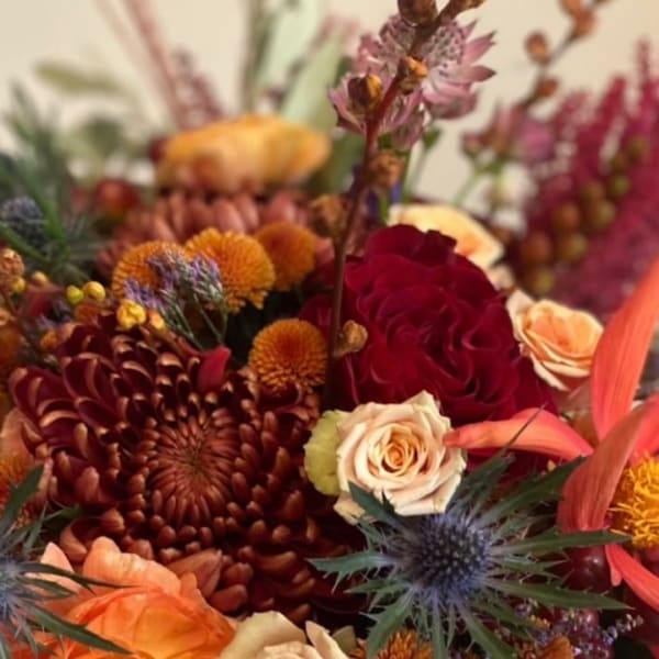 Autumn bouquet with red and peach roses, orange mums, and thistle-like blooms
