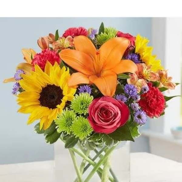 Colorful bouquet with sunflowers, lilies, and roses in a clear glass vase