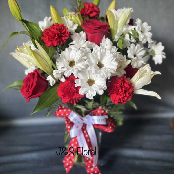 Bouquet of red roses, white daisies, and red carnations in a glass vase