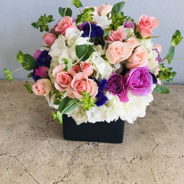 Mixed pink, white, and purple flower arrangement in a black box
