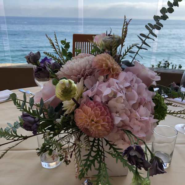 Pastel floral centerpiece in a low square vase on a table by the water