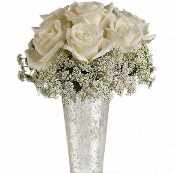 White roses in a tall silver vase with baby's breath