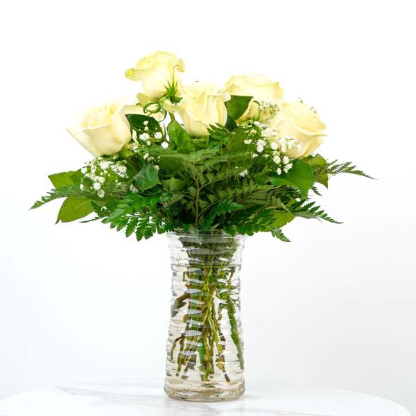 Tall clear glass vase of pale yellow roses with baby's breath accents