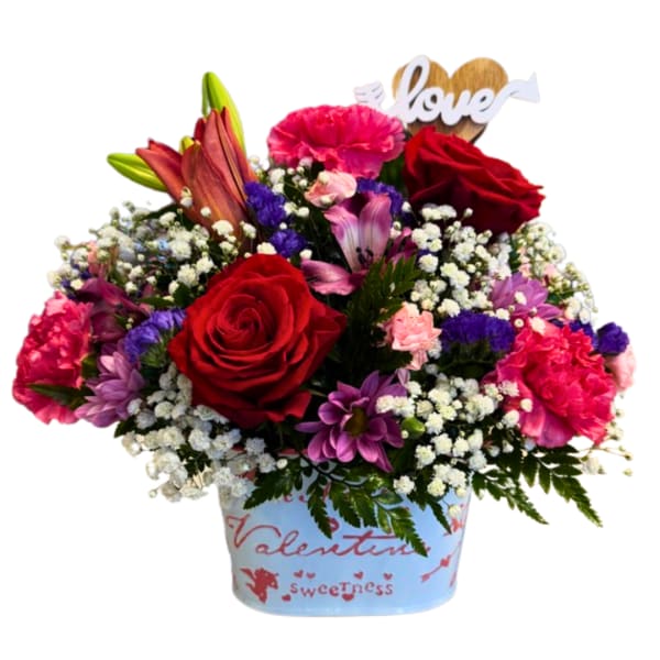 Mixed bouquet of red roses, lilies, and pink carnations in a decorated container