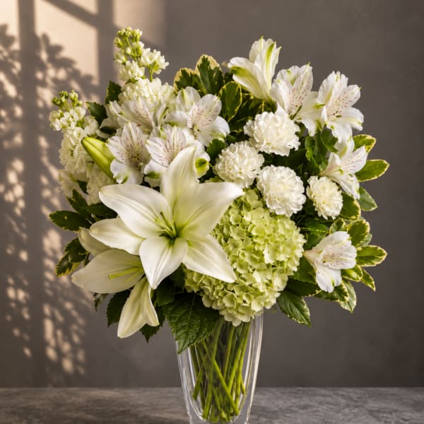 White lilies and mixed white flowers in a clear glass vase
