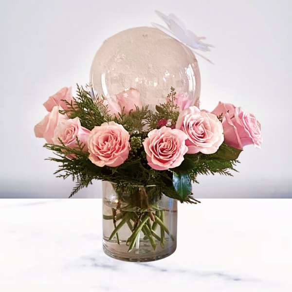 Pink roses arranged in a clear glass vase with a large clear balloon above