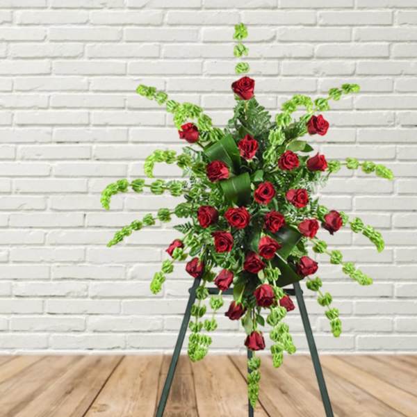 Standing floral spray of red roses with trailing green foliage on an easel