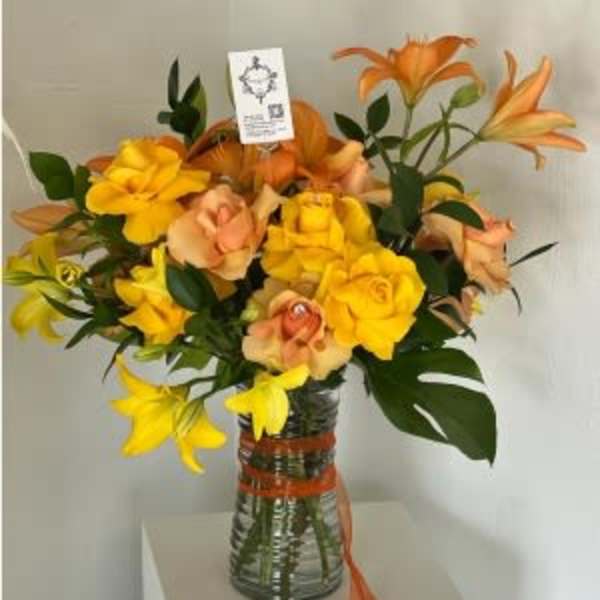 Orange and yellow lilies arranged in a glass vase with ribbon
