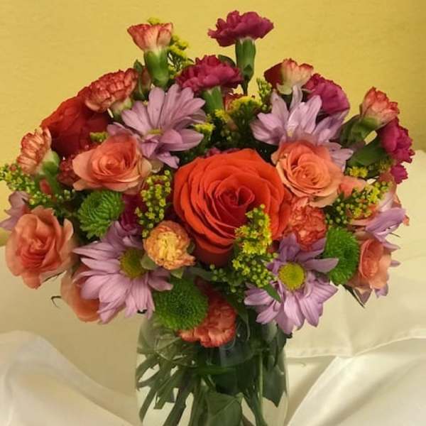 Mixed bouquet of roses, carnations, and purple daisies in a glass vase