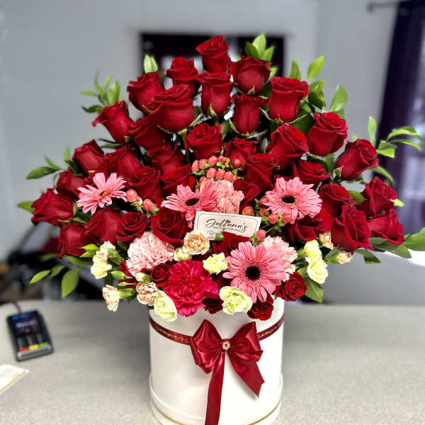 Red roses and pink flowers arranged in a white hat box with a red ribbon