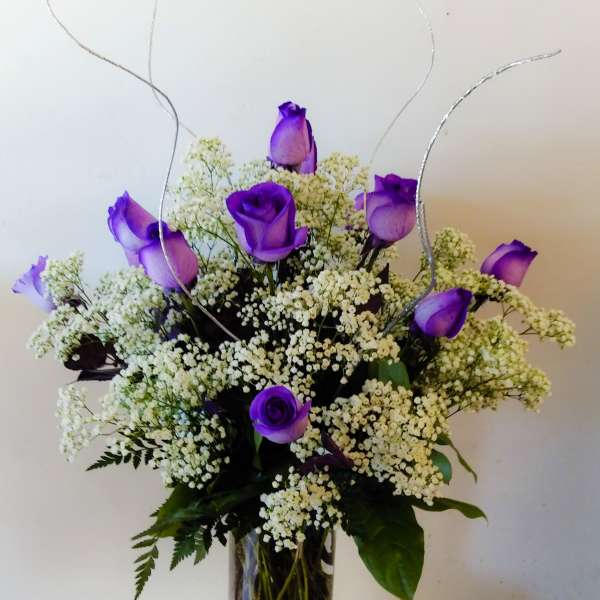 Purple roses in a glass vase with white filler flowers