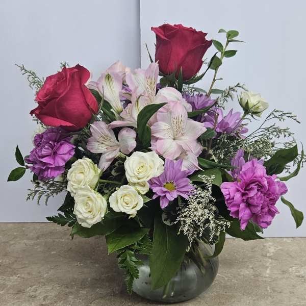 Mixed bouquet of roses, lilies, and purple flowers in a glass vase