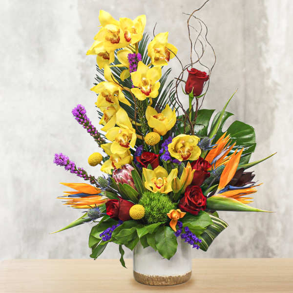 Tall tropical bouquet with yellow orchids, red roses, and orange bird-of-paradise in a glass vase