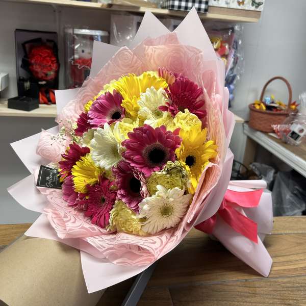 Bouquet of pink, yellow, and white gerbera daisies wrapped in pink paper