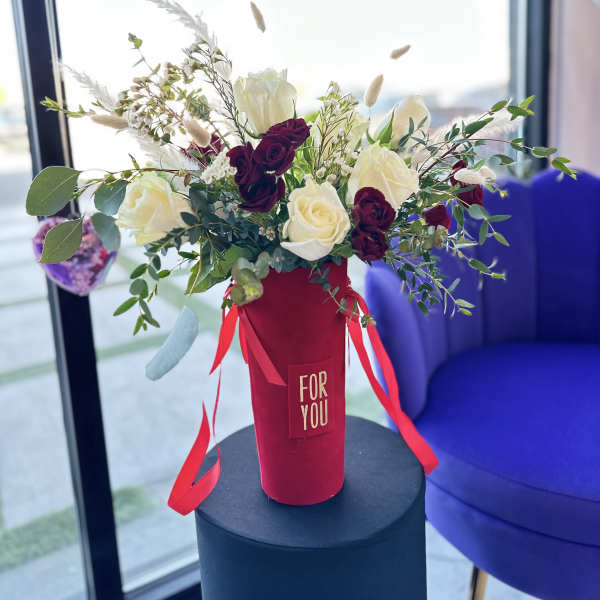 Red and white rose arrangement in a tall red box with ribbon