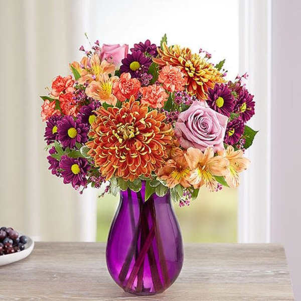 Mixed bouquet of purple, orange, pink, and peach flowers in a purple vase