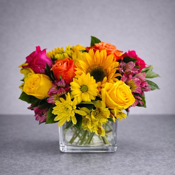 Colorful bouquet of roses, sunflowers, and daisies in a clear glass vase