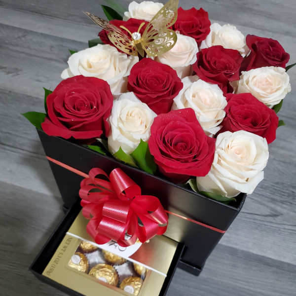 Red and white roses in a black gift box with chocolates and a ribbon