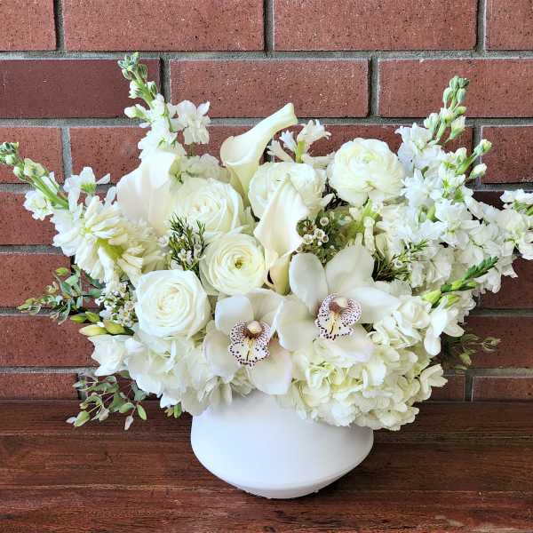 White floral arrangement in a white vase with roses and orchids