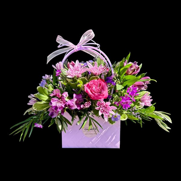Pink and purple mixed flower arrangement in a lavender gift bag with ribbon handle