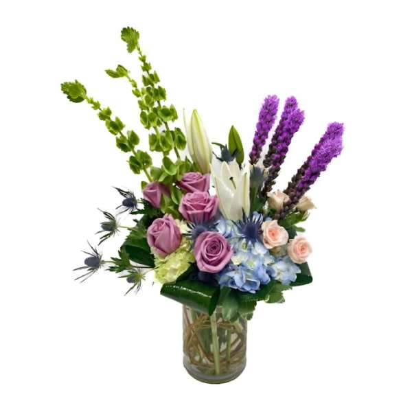 Tall mixed arrangement with purple liatris, lavender roses, white lilies, and blue hydrangea in a glass vase