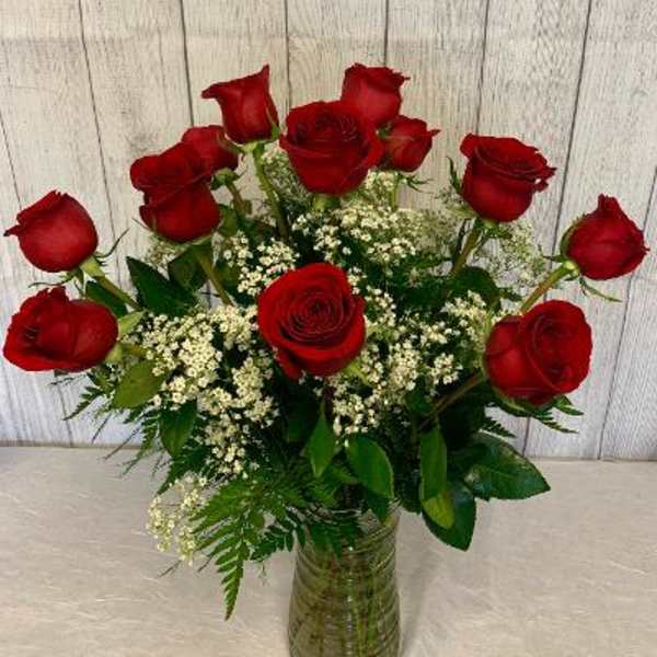 Red roses arranged in a glass vase with white filler flowers