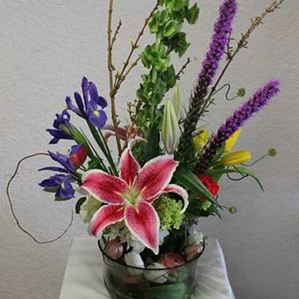 Tall mixed flower arrangement with a pink lily in a glass bowl