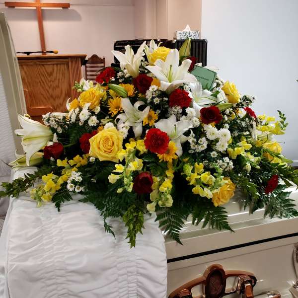 Large casket spray with white lilies, red and yellow roses, and yellow flowers