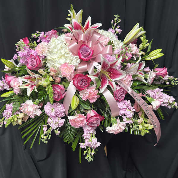 Pink and white floral spray with lilies, roses, and ribbon on a black backdrop
