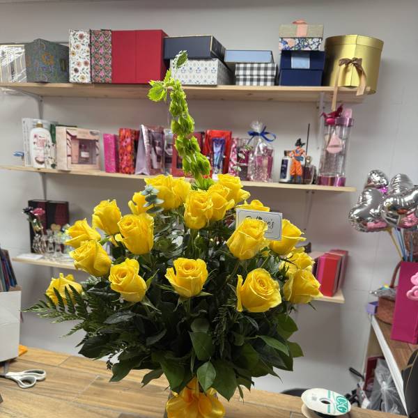 Yellow roses arranged in a glass vase with a yellow ribbon.