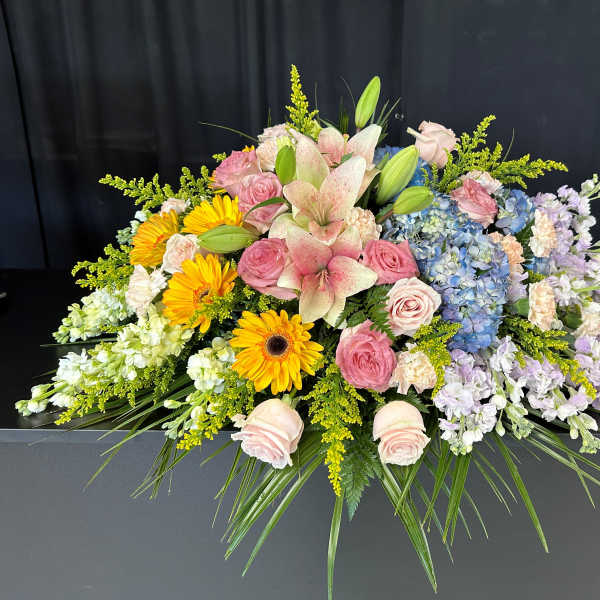 Large floral casket spray with pink roses, lilies, hydrangeas, and yellow daisies