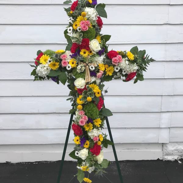 Cross-shaped floral tribute on a stand with mixed bright flowers