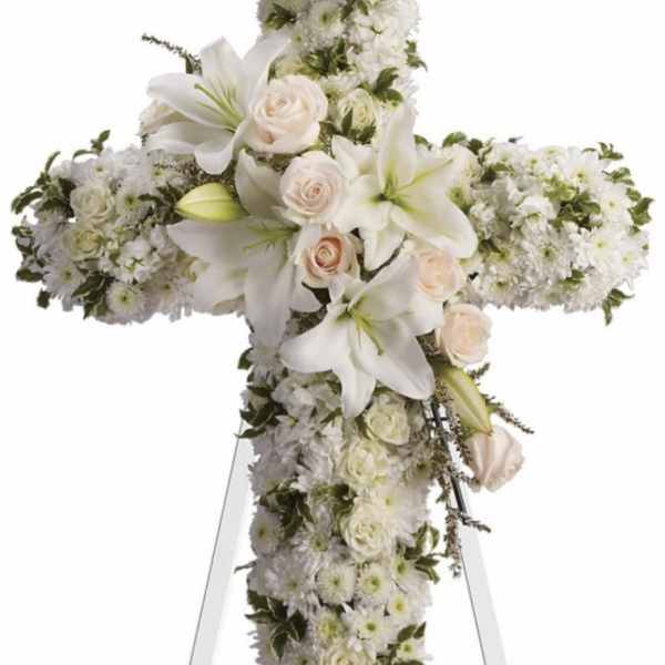 White floral cross on an easel with roses and lilies