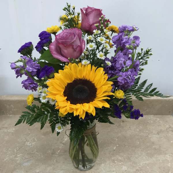 Bouquet with sunflowers, pink roses, and purple flowers in a glass vase