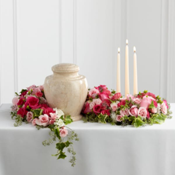 Pink rose centerpiece with a beige urn and three taper candles