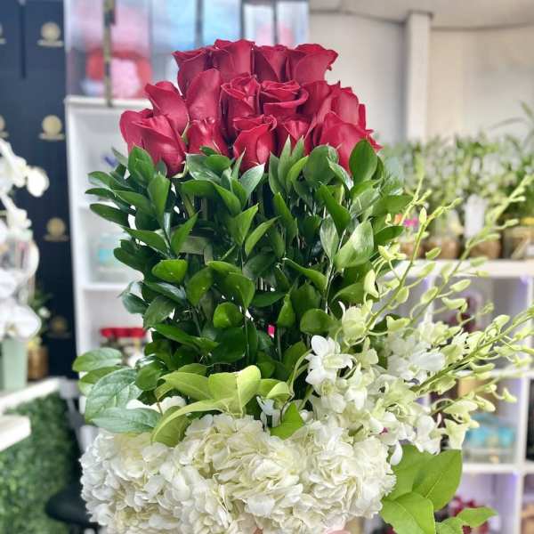 Tall arrangement of red roses and white hydrangeas in a gold hat box with pink ribbon