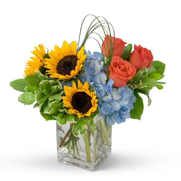 Sunflowers, blue hydrangeas, and coral roses in a clear glass vase
