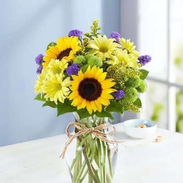Sunflowers and yellow daisies in a clear glass vase with a twine bow
