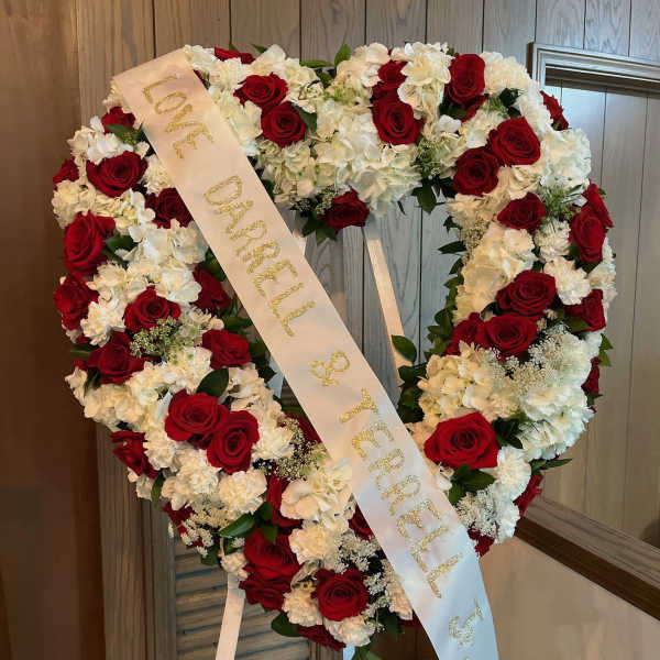 Heart-shaped wreath of red roses and white flowers with a memorial ribbon