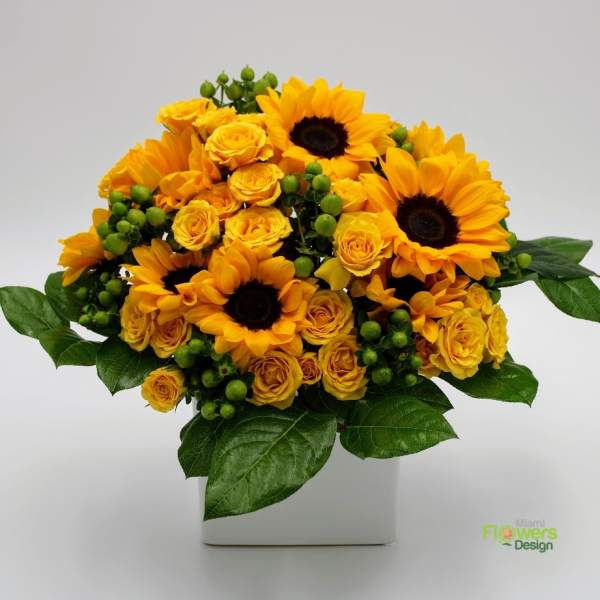 Yellow sunflowers and roses arranged in a white square vase